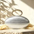Silver oval clutch bag featuring crocodile texture and stylish metal ring handle for parties. - Silver