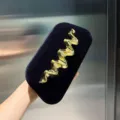Detailansicht einer eleganten schwarzen Samt-Clutch mit goldener Metallic-Wellen-Dekoration. - Schwarz