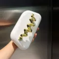 Nahaufnahme der weißen Hartschalen-Clutch mit matter Textur und edlem goldenen Wellen-Akzent. - Weiß