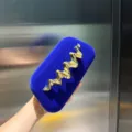 Detailaufnahme der blauen Samt-Box-Clutch mit auffälligem goldenem Wellen-Metalldesign. - Blau