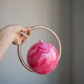 Detailansicht einer stilvollen runden Abendtasche mit rosa Marmormuster und goldenem Ringgriff. - Fluid Rosarot