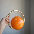 Elegante kugelformige Abendtasche mit orangenem Marmormuster und luxuriosem Goldringgriff. - Fluid Orange