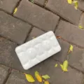 Detailansicht der glänzenden weißen Acryl-Puff-Clutch mit goldenem Verschluss auf Stein. - Flüssiges Weiß