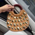 Detail view of trendy canvas handbag with wooden handle and unique gold metallic stone studs. - Amber