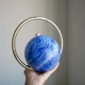 Stilvolle kugelförmige Abendtasche mit blauem Marmormuster und vergoldetem Ringgriff. - Fluid Blau