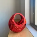 Detailed view of the red metallic glossy acrylic handbag featuring unique ribbed swirl texture. - Red