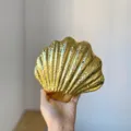 Nahaufnahme der goldenen Muschel-Abendtasche mit glänzender, strukturierter Wellenoberfläche. - Gold