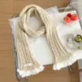Vista detallada de la bufanda de punto crema con un delicado borde de encaje blanco. - Beige