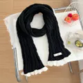 Close-up detail of black knitted scarf with delicate white lace trim, cozy winter fashion. - Black