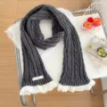 Close-up of dark grey cable knit scarf featuring delicate white lace trim and woven label. - Dark Gray