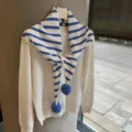 Detailed view of fashionable striped knitted scarf with pom-poms matching a cozy white sweater. - 135x80cm / Blue and White Stripes