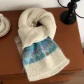 Detail view of a cozy warm knitted winter scarf with floral pattern on a retro wooden table. - 160x22cm / Beige