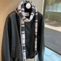 Vista detallada de bufanda de lana a rayas estrecha sobre chaqueta de cuero en un ambiente elegante - Gris Y Blanco