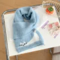 Primo piano dettagliato della sciarpa invernale in morbido filato azzurro con ricamo. - Gatto Pigro - Blu