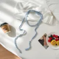 Detailed view of handmade light blue crochet long scarf or necklace accessory on white bed. - Light Blue