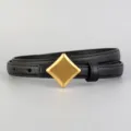Detail view of women's black leather belt featuring a vintage gold diamond buckle. - Black