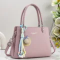 Detailansicht der stilvollen pinkfarbenen Schultertasche mit Hutanhänger und feiner Textur. - Rosa