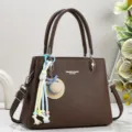 Nahaufnahme einer dunkelbraunen Lederhandtasche mit schickem Strohhutanhänger und Details. - Kaffeebraun