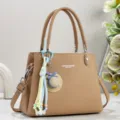 Nahaufnahme der khakifarbenen Ledertasche mit schickem Strohhut-Anhänger und Metallbeschlägen. - Khaki