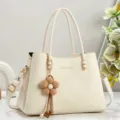 Detailed view of cream handbag with elegant flower charm, double handles and shoulder strap. - Off White