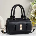 Close-up detail of a black leather handbag featuring gold-tone hardware and unique lock. - Black