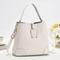 Schickes beige Leder Eimerbeutel Detail mit Goldbeschlägen und stylischem Front Metalllogo. - Weiß