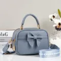 Detailopname van stijlvolle blauwe leren crossbodytas met elegante strik en brede band. - Lichtblauw