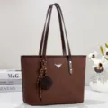 Dettaglio borsa shopper in pelle marrone, con doppi manici a spalla e ciondolo chic. - Caffè