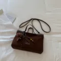 Detailaufnahme einer dunkelbraunen Wildleder-Umhängetasche mit Karomütze und Perlen. - Mit Anhänger / Kaffee