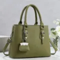 Primer plano del bolso de mano de cuero verde oliva con diseño estructurado y dije en miniatura. - Verde