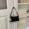 Λεπτομερής εικόνα μινιμαλιστικής μαύρης τσάντας ώμου με χαριτωμένο μενταγιόν. - Με Μενταγιόν / Μαύρο