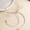 Primer plano detalle de un cinturón fino de piel beige minimalista con elegante lazo. - Dorado con Blanco
