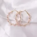 Close-up detail view of elegant pink crystal twisted hoop earrings on soft white satin. - Regular Style (ES3662) / Pink Rhinestone Embellished Style