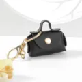 Gros plan détail du mini porte-clés sac en cuir, quioncaillerie dorée, bouton pression. - Noir
