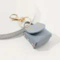 Gros plan sur le porte-clés mini sac chat en cuir PU gris avec des accessoires métalliques dorés. - Bleu clair