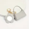 Gros plan détail du mini sac à main en cuir gris et du porte-clés miroir fleur. - Sac Courbé + Miroir Fleur / Gris