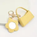 Gedetailleerde close-up van gele lederen mini hobo tas sleutelhanger met bloem spiegel. - Gebogen Tas + Bloemen Spiegel / Geel