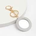 Vue détaillée du porte-clés miroir de poche rond en cuir élégant doté d'une quincaillerie dorée. - Gris