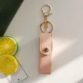 Gros plan sur l'étui à rouge à lèvres en cuir rose avec bouton-pression et anneau doré. - Rose
