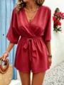 Elegant V-neck solid color short romper with waist tie in a scenic outdoor setting, detail view. - Red