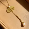 Close-up detail of the elegant gold lace petal pearl lariat necklace resting in a box. - Necklace / Gold