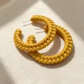 Close-up of unique braided leather textured C-hoop earrings in vibrant yellow, detail view. - Yellow