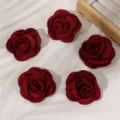 Detailed close-up of dark red fabric rose hair clips arranged on a textured white background. - Red
