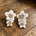 Exquisite asymmetric flower stud earrings with white enamel and golden pistil details. - White