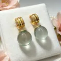 Detailed close-up of C-shaped gold tone earrings with light green crystal sphere drops. - Light Green