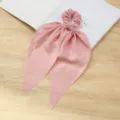 Gedetailleerd uitzicht roze lint haarelastiek met zachte stoftextur en elegant lang striemontwerp. - Roze