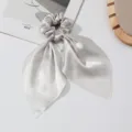 Gedetailleerde close-up van de elegante zilveren satijnen haarelastiek met lange linten. - Zilverijs