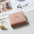 Primo piano dettaglio del portafoglio corto in pelle rosa con ciondolo margherita in metallo e zip. - Rosa chiaro