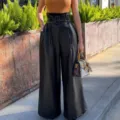 High-waist black PU leather wide-leg pants detail, showing metal buckle belt and texture. - S / Black