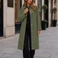 Vue détaillée en scène extérieure présentant un élégant manteau long vert olive à revers. - S / Hauts / Vert